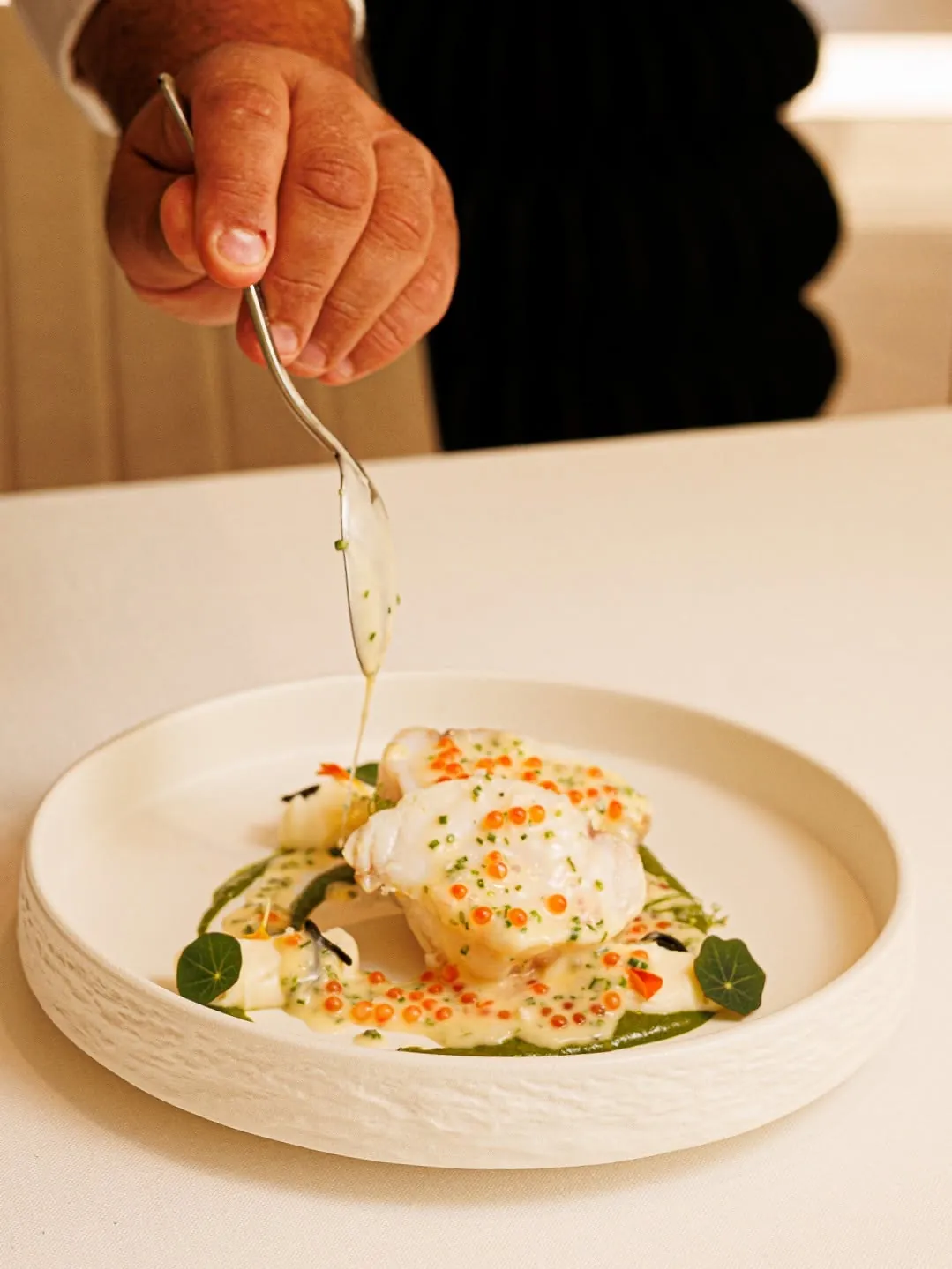 A sauce being spooned over a fish dish at the pass