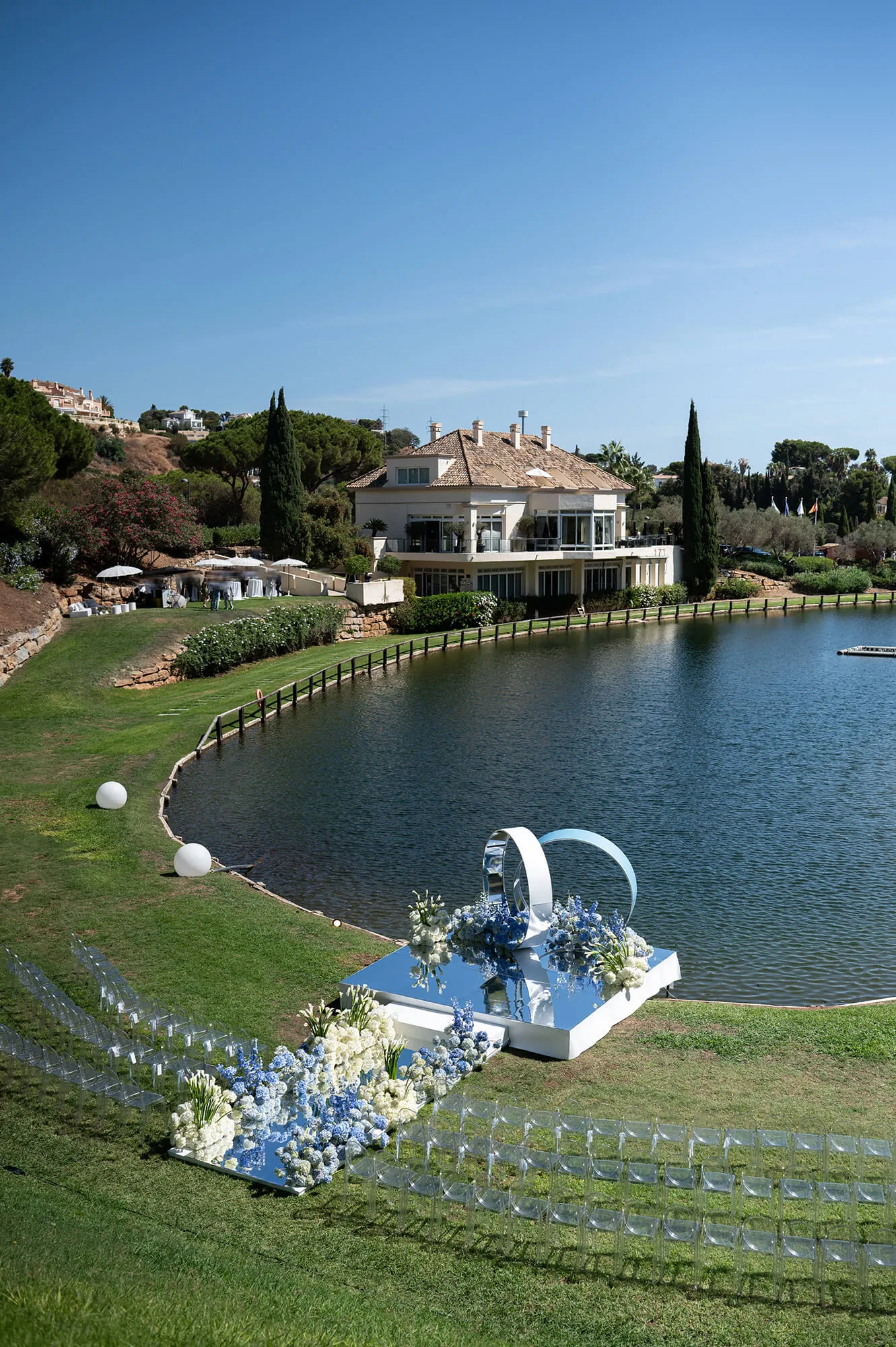 A wedding ceremony set up on the lawn beside the lake, with the clubhouse behind